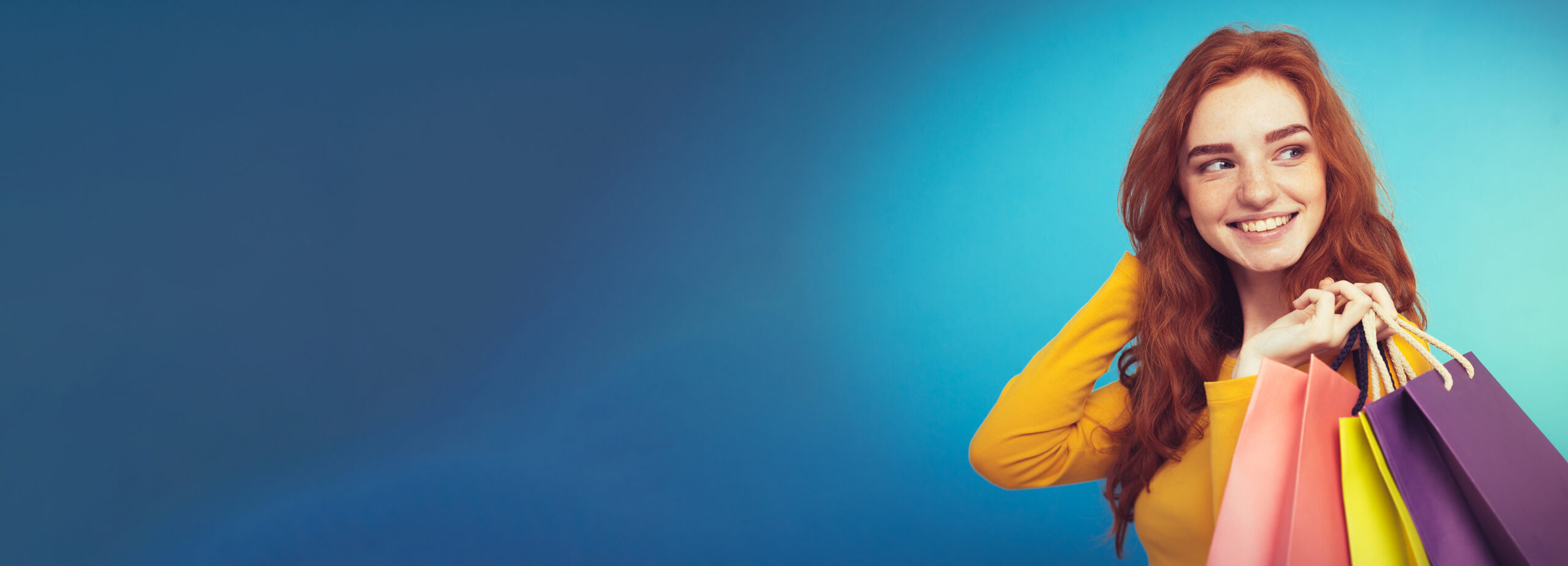 Shopping Concept - Close up Portrait young beautiful attractive redhair girl smiling looking at camera with shopping bag. Blue Pastel Background. Copy space.